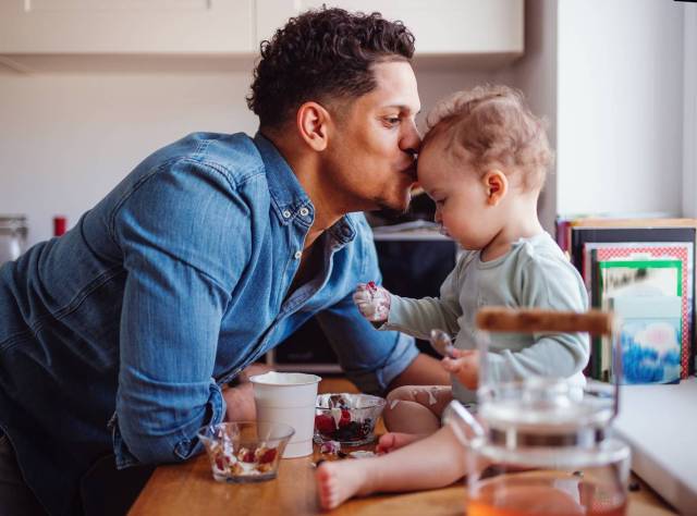 a dad kisses his baby on the forehead, baby sitting on the counter, playing games for babies