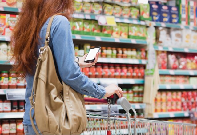 woman in store with shopping cart looking at phone