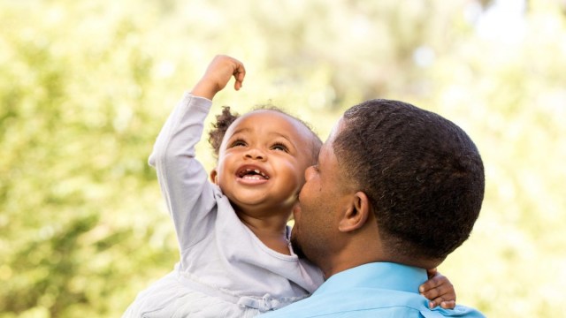 A father holds his daughter up to his cheek on a sunny day