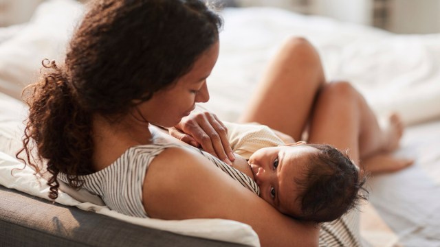 a woman breastfeeding her baby in bed for a story on the best breastfeeding positions