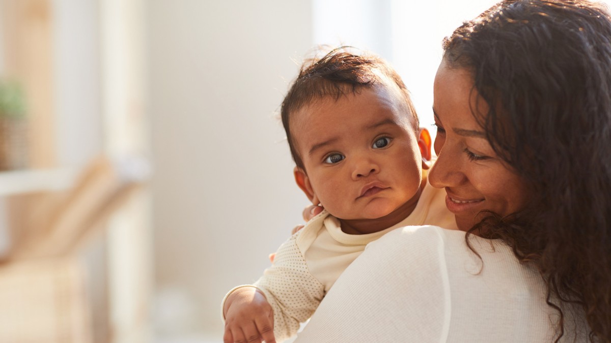 a baby looks over his mom's shoulder, holding up his head