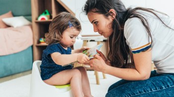 a little girl sitting on the potty beside her mom, who now knows when to start potty training and common mistakes to avoid